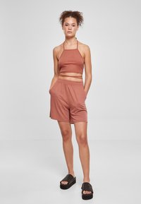 Rustfarget, rillet crop-top med tynne stropper, kombinert med løse shorts til knærne og svarte platå-sandaler. Glatt stoff, uformell design.