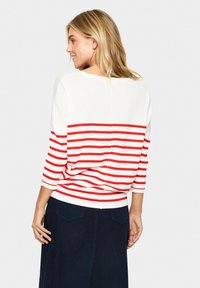 Pull rayé avec des lignes horizontales blanches et rouges, manches trois-quarts, col bateau, et coupe décontractée. Tissu en tricot léger.