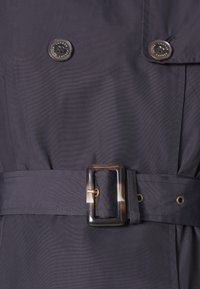 Mörkgrå trenchcoat med två glänsande knappar, ett brett bälte med en unik spänne och ett glatt, texturerat tyg.