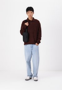 Maglione marrone con texture e colletto, jeans chiari a gamba larga, borsa a tracolla nera e sneakers grigie/white. Sfondo semplice.