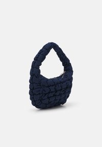Petit sac à main matelassé bleu marine avec une poignée rembourrée et une fermeture éclair en argent visible sur un fond blanc.