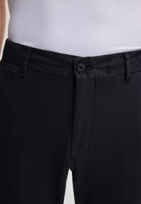 Czarne spodnie o gładkiej fakturze, z zapięciem na guzik, zamkiem błyskawicznym i bocznymi kieszeniami. Prosty fason z prostymi nogawkami.