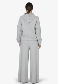 Lichtgrijze hoodie en wijde broek set gemaakt van zachte, textuurstof. Heeft een capuchon en een relaxte pasvorm met zichtbare stikseldetails.