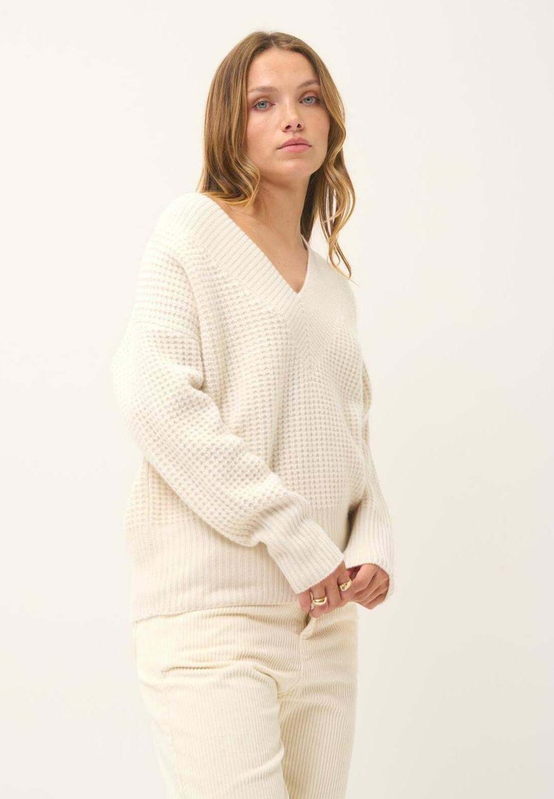 Cremefarbenes, oversized V-Ausschnitt-Pullover mit strukturiertem Strickmuster und Rippbündchen, kombiniert mit passenden, gerippten Cremepants.