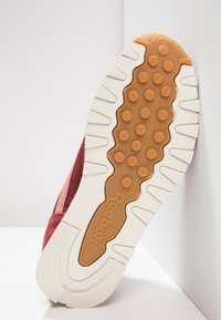 Semelle de basket Reebok avec une semelle extérieure en caoutchouc texturé de couleur beige clair, une semelle intermédiaire blanche et une tige en tissu rouge intégrant des accents en mesh et en daim.