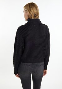 Schwarzer Strickpullover mit hohem Kragen, ribbelter Textur, langen Ärmeln und lockerer Passform, kombiniert mit dunklen Jeans.