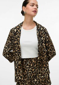 Blazer v leopardím vzoru vyrobený z měkké látky, s volným střihem, otevřeným předním dílem a dvěma předními kapsami, zkombinovaný s bílým crop topem pod ním.