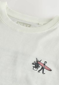 Col de t-shirt blanc et haut de poitrine avec broderie représentant une personne portant une planche de surf rose à côté d'une plante en pot.