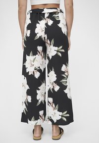 Bukser med vide ben, med svart base og store hvite og rosa blomster, belte i livet og et teksturert stoff.