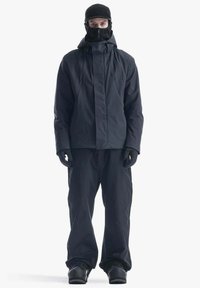 Giacca e pantaloni neri impermeabili con colletto alto, guanti e cappello aderente. Texture liscia, design minimalista e copertura totale.