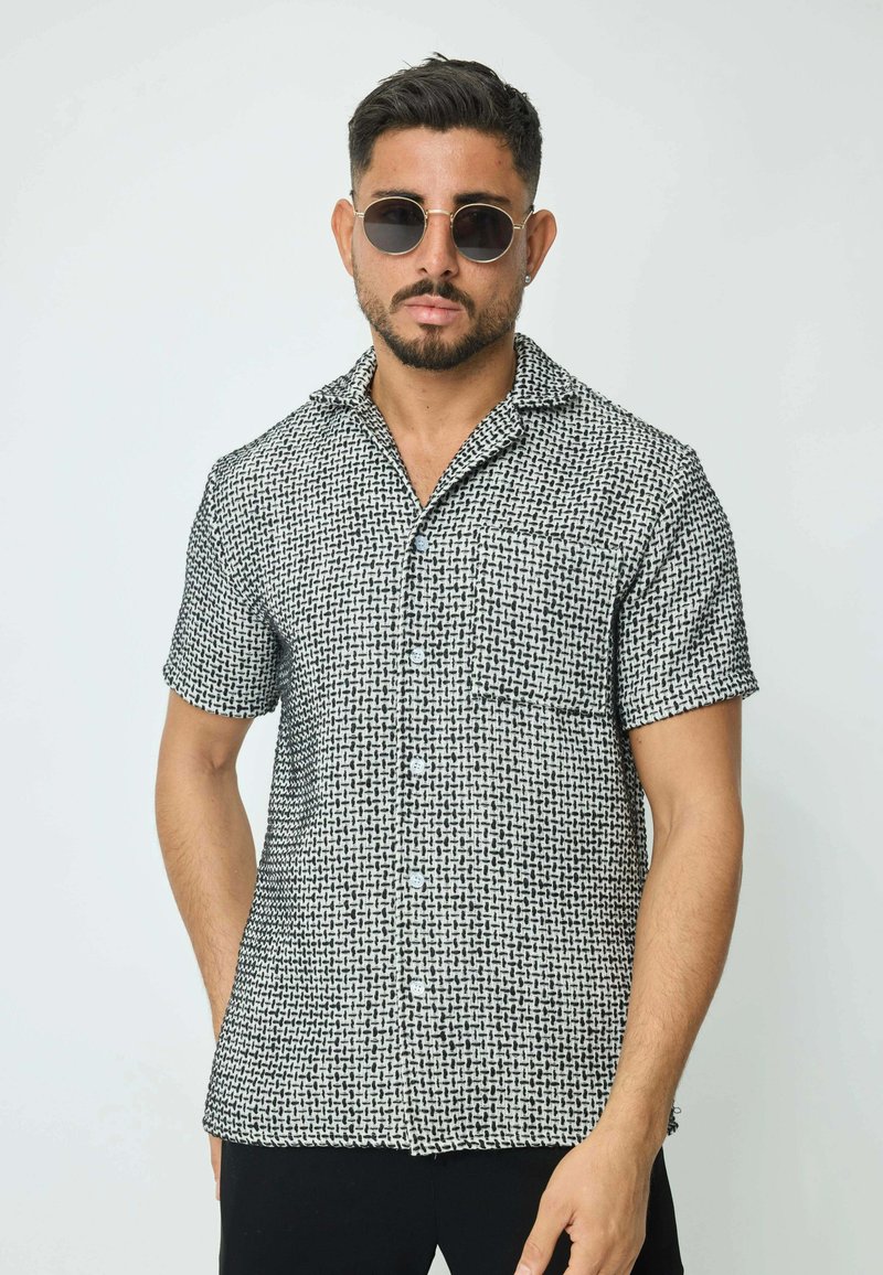 Chemise à manches courtes au motif tissé noir et blanc, dotée d'un col, d'une fermeture à boutons et d'une poche poitrine sur un fond uni.