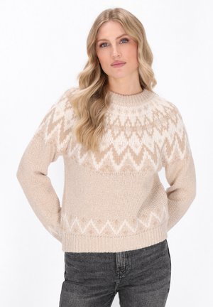 Maglione beige chiaro con motivo a zigzag bianco, collo rotondo e maniche lunghe. Realizzato in un morbido tessuto testurizzato. Abbinato a jeans scuri.