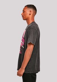 Black graphic t-shirt made of cotton, featuring a colorful design on the front, short sleeves, and a relaxed fit. Worn with dark pants.
