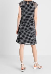 Vestido de estampado en blanco y negro con dobladillo acampanado, mangas cortas y detalle de ojal en la espalda, acompañado de sandalias blancas de tiras.