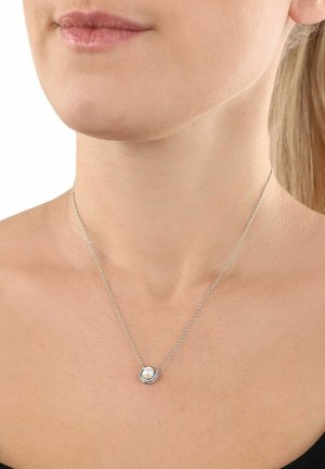 Donna che indossa una delicata collana in argento con un piccolo pendente a perla rotonda sulla clavicola.