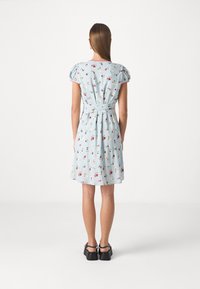 Rochie florală albastră cu mâneci bufante, talie ajustată și curea legată. Are un material ușor și o fustă evazată până la genunchi. Pantofi negri.