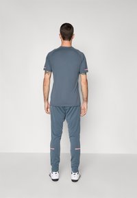 T-shirt de sport gris à manches courtes avec des poignets contrastés, associé à un pantalon ajusté assorti avec des accents rouges et blancs.