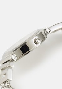 Ατσάλινο μεταλλικό ρολόι χειρός με λείο bezel, υφασμένη κορώνα και βραχιόλι αλυσίδας, αναδεικνύοντας κομψές γραμμές και γυαλιστερές επιφάνειες.