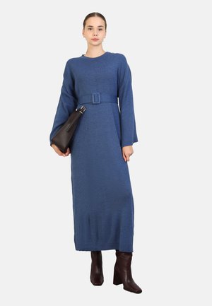 Blue ribbed long dress with a belt, featuring long sleeves and a straight silhouette. Paired with brown heeled boots and a dark handbag.