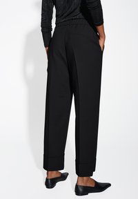 Pantaloni neri con una vestibilità rilassata, dotati di una cintura in vita, tasche laterali e orli risvoltati. Tessuto liscio con una finitura opaca.