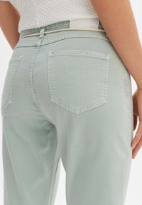 Pantaloni in denim verde chiaro con vita alta, dotati di tasche posteriori e dettagli di cucitura sottili. Il tessuto ha una finitura liscia e leggermente textured.