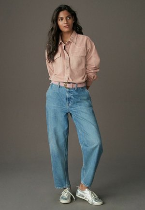 Helles rosa Hemd mit zwei Brusttaschen, kombiniert mit lockeren hellblauen Jeans und silbernen Sportschuhen. Schlichtes, lässiges Design.