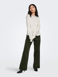 Crèmekleurig gebreid vest met een ronde hals, voorzien van knopen aan de voorkant en een gerimpelde zoom. Gecombineerd met donkergroene corduroy wijde pijpen broek en zwarte hakken.