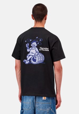 Mand set bagfra iført en sort t-shirt med en tegneserie af en mand, der holder et glas og sidder på et fad med teksten The Action Is The Juice.