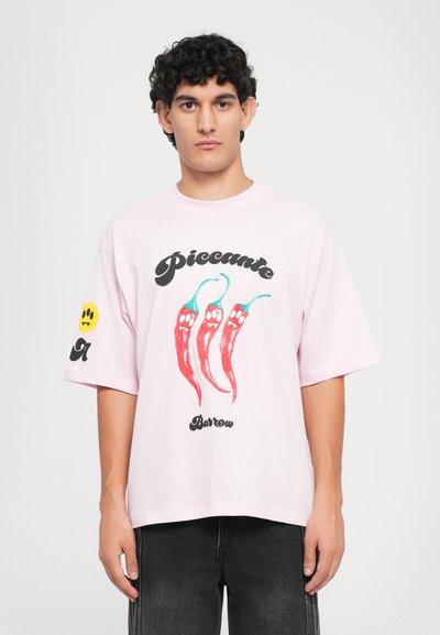 Ružové oversize tričko vyrobené z bavlny, s tromi grafikami červených chilli papričiek a čiernym textom, s akcentom smajlíka na rukáve.