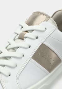 Άσπρο αθλητικό παπούτσι με μπεζ λεπτομέρειες, υφασμένο κορδόνι και γλώσσα, λείο συνθετικό επάνω μέρος και οπές στο πλάι για αερισμό.