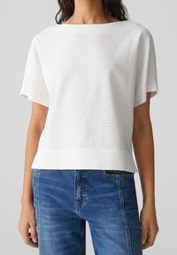 Hvid tekstureret kortærmet top med bådhals, parret med blå denim jeans. Stoffet har et subtilt vævet mønster.