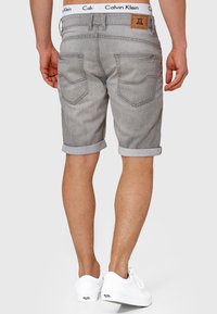 Harmaat farkkushortsit, joissa on käännetyt lahkeet, kaksi takataskua ja Calvin Klein -logopatchi vyötäröllä. Yhdistetty valkoisiin tennareihin.