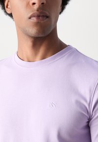 Lilla bomull t-skjorte med rund hals, med liten brodert logo på brystet, glatt tekstur og korte ermer.