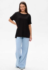 Czarna koszulka z krótkim rękawem o luźnym kroju i bocznymi rozcięciami, zestawiona ze jasnoniebieskimi dżinsami w stylu dzwonów. Gładka faktura, casualowy design.