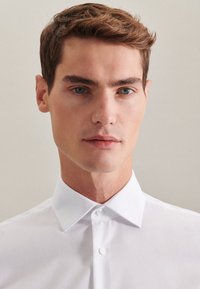 Camicetta bianca con colletto classico, realizzata in tessuto morbido. Presenta linee pulite e un design aderente, che valorizza un look curato.