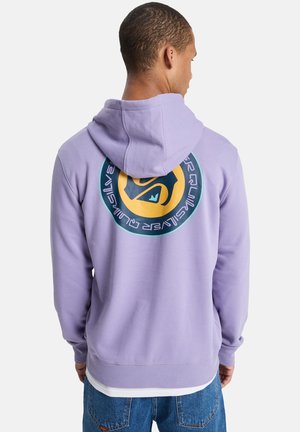 Fioletowa bluza z kapturem z okrągłą grafiką na plecach, z żółtym środkiem i turkusowymi akcentami. Miękki materiał, luźny krój.