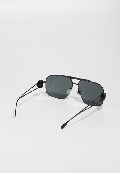 Lunettes de soleil noires rectangulaires avec des verres gris foncé, monture en métal mince et branches droites. Présente des accents ronds près des charnières des tempes.