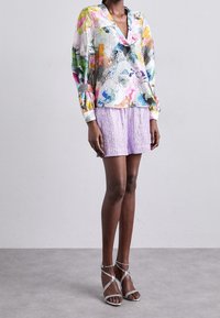 Multicolored textured blouse with a V-neck and structured sleeves paired with a lilac pleated skirt and silver strappy high-heeled sandals.