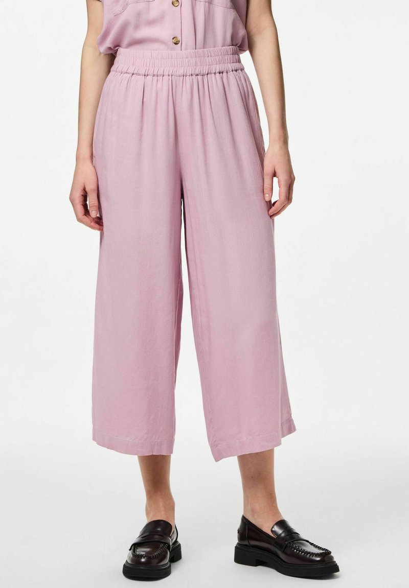 Pantalones anchos de color rosa claro con cintura elástica y tejido texturizado, combinados con mocasines oscuros, que muestran un ajuste casual y relajado.
