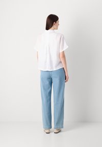 Blusa branca de manga curta com colarinho, combinada com jeans de ganga de corte solto em azul claro e calçado bege. Design simples e limpo.