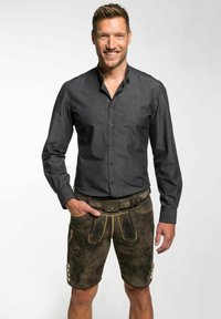 Donkergrijze, langermige blouse met knopen, gecombineerd met bruin leren shorts met borduurwerk en decoratieve knopen, gedragen met een riem.