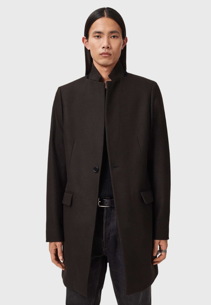 Tummanruskea villakangas takki, jossa on korkea kaulus, yksittäinen nappisuljenta, kaksi etutaskua, suora leikkaus ja sileä rakenne.