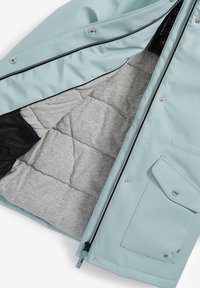 Veste imperméable bleu clair avec doublure grise matelassée, poche en maille noire, boutons-pression et fermetures éclair. Comprend une poche avant.