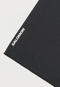 Μαύρο ύφασμα με λευκό λογότυπο "SALOMON" τυπωμένο κοντά στην ραμμένη άκρη πάνω σε ανοιχτό φόντο.