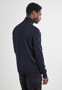 Pull en maille bleu marine avec col montant, poignets et ourlet côtelés, offrant une texture lisse et un design minimaliste.
