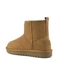 Hnědá semišová kotníková bota s měkkou kožešinovou podšívkou, kulatou špičkou a gumovou podrážkou s cikcakovým vzorem. Obsahuje malou poutko vzadu.