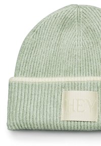 Groene gebreide beanie met een geribbelde structuur, een opgerolde rand en een crèmekleurige streep. Inclusief een stoffen label met "HEY" erop gedrukt.
