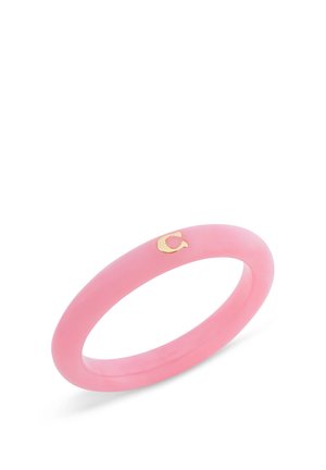 Bracelet jonc en résine rose avec un petit détail lettre « C » en or sur fond blanc.