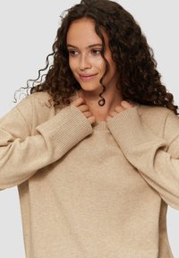 Beige trui gemaakt van zacht breimateriaal, met een geribbelde halslijn en manchetten, een ontspannen pasvorm en een lichte textuur overal.