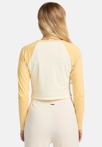 Geknipte lange mouwen top met een gele raglan ontwerp, een roomkleurig lichaam, zacht materiaal en minimale stikdetails aan de zoom.
